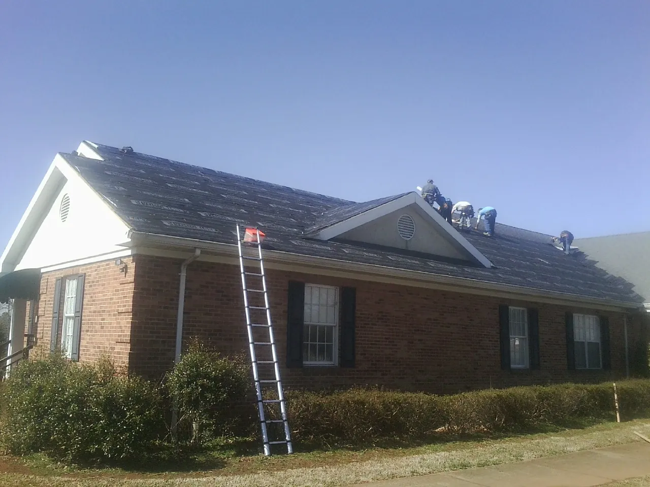 Crew tearing shingles off a brick ranch roof with a ladder set — Emergency Roof Repair work by our crew in Lake Forest