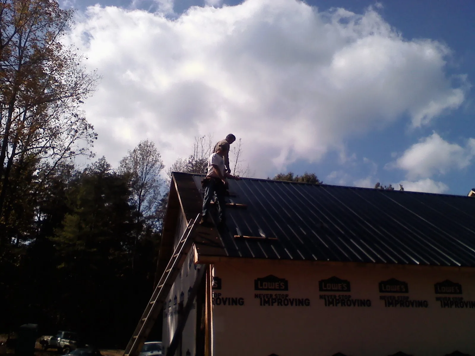 Roofer fastening dark metal panels high against a cloudy sky, from a Roof Inspection job in Lake Forest